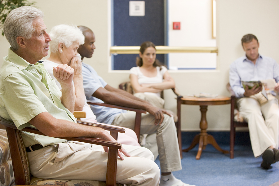 A crowded waiting room with wooden chairs and blue carpet.