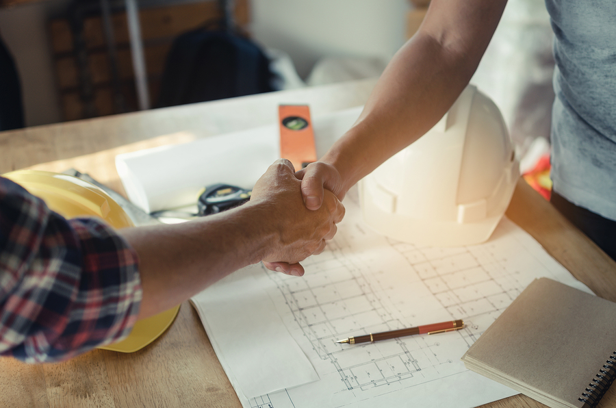 Two people shaking hands over blueprints. 